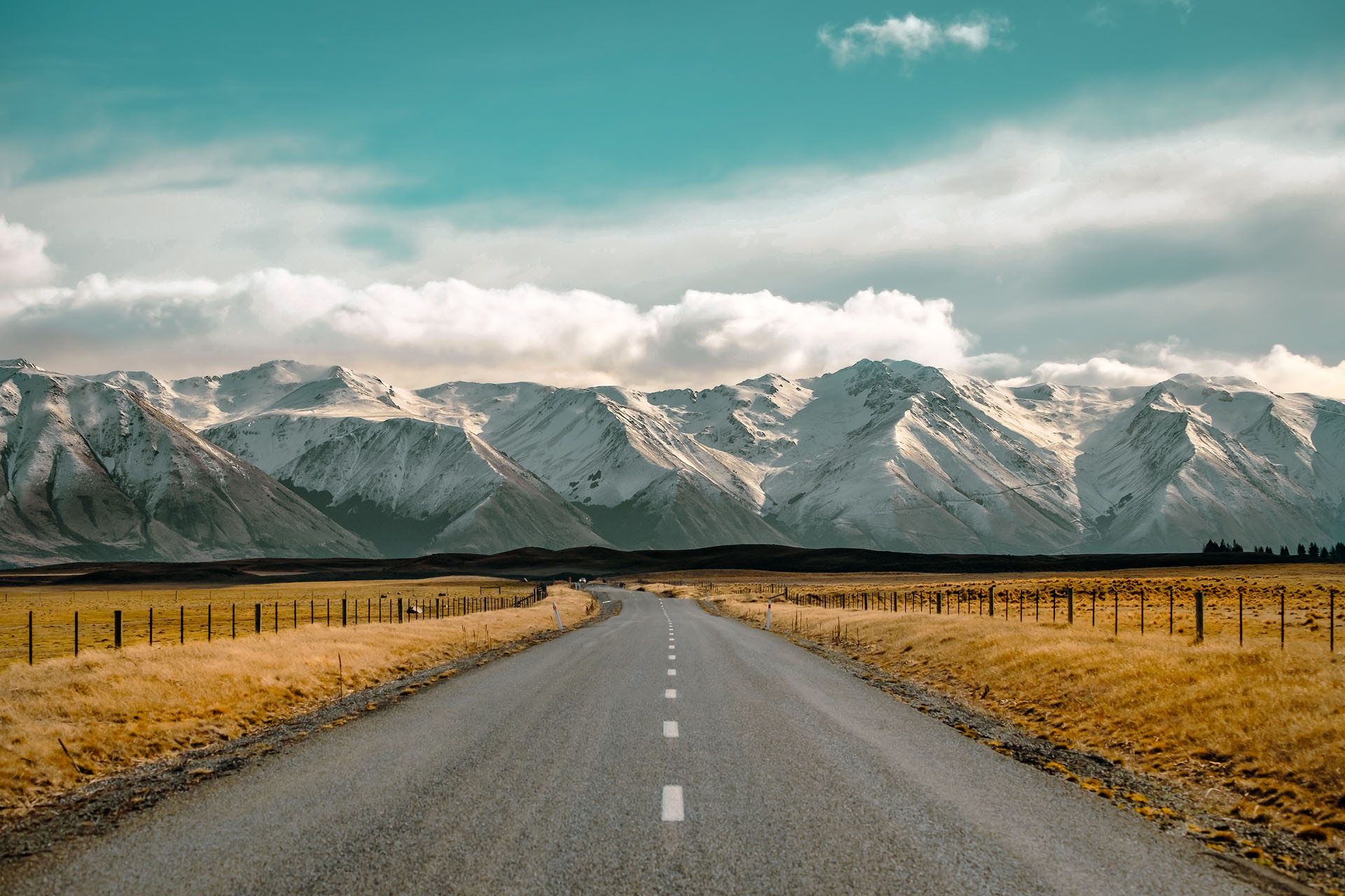 A Long Straight Road Leading Towards A Snow Capped Mountain In N